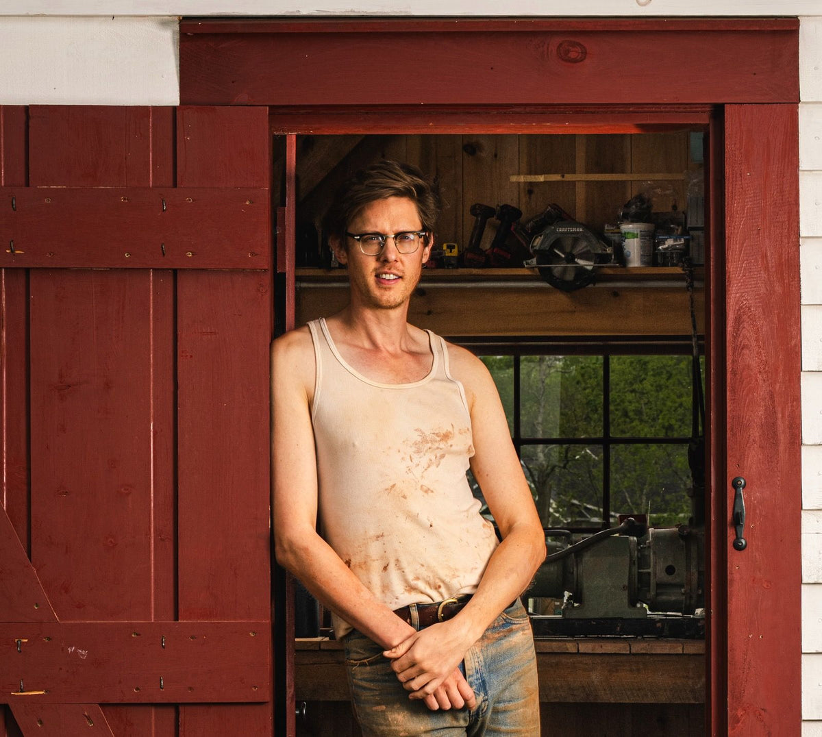 John standing and leaning on the doorway of his small white cabin pottery studio.