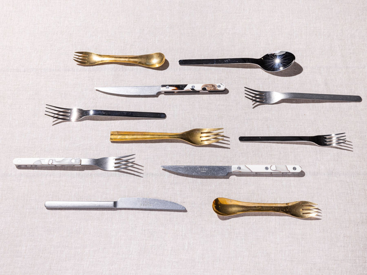Different styles of forks, spoons, and knifes artfully lined up in parallel rows.
