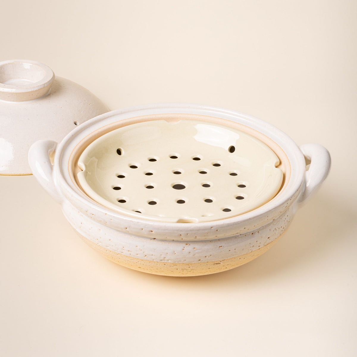 White ceramic donabe steamer with side handles, a steamer tray and a lid to the side.