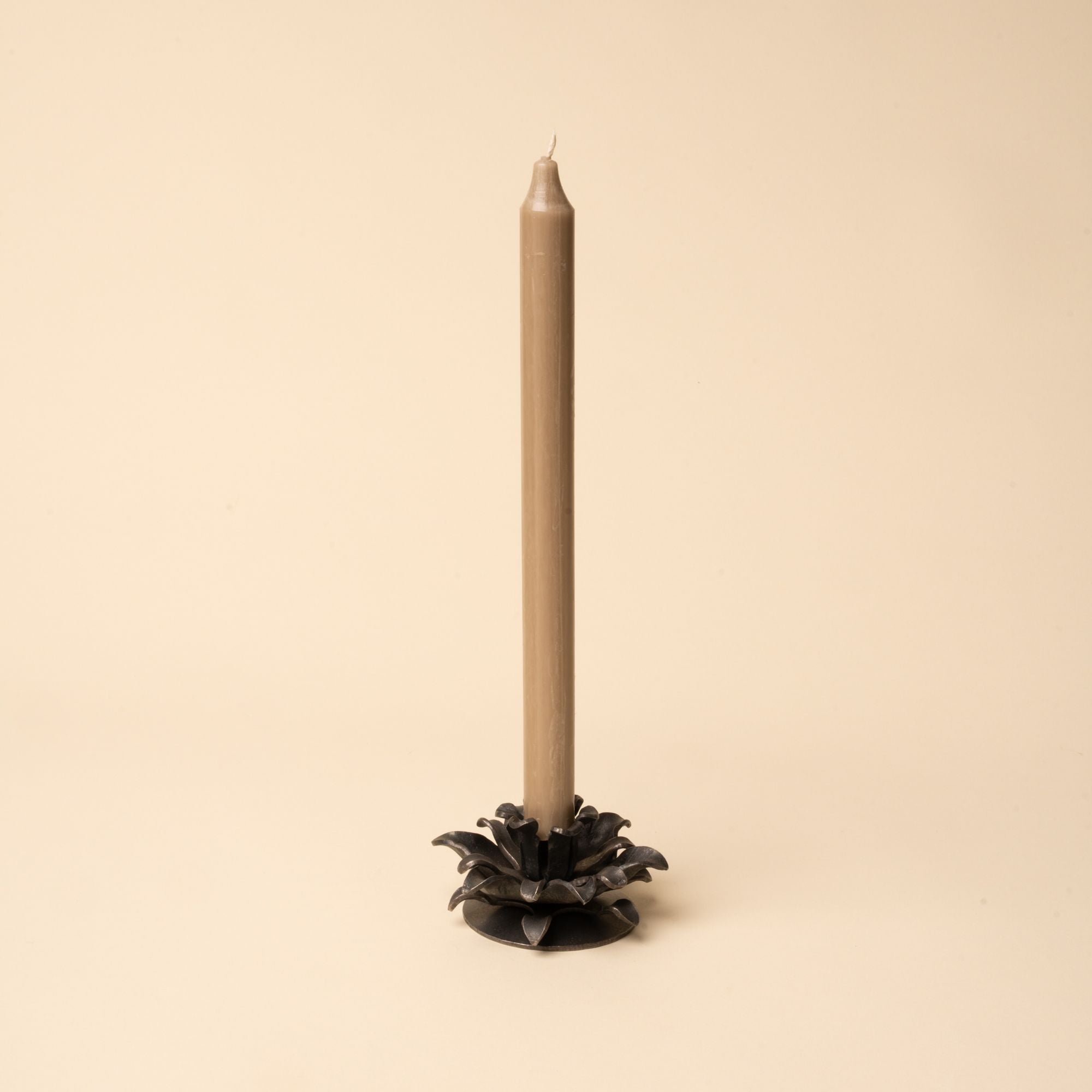 Brown taper candle in an iron holder shaped like layered flower petals, set against a beige background.