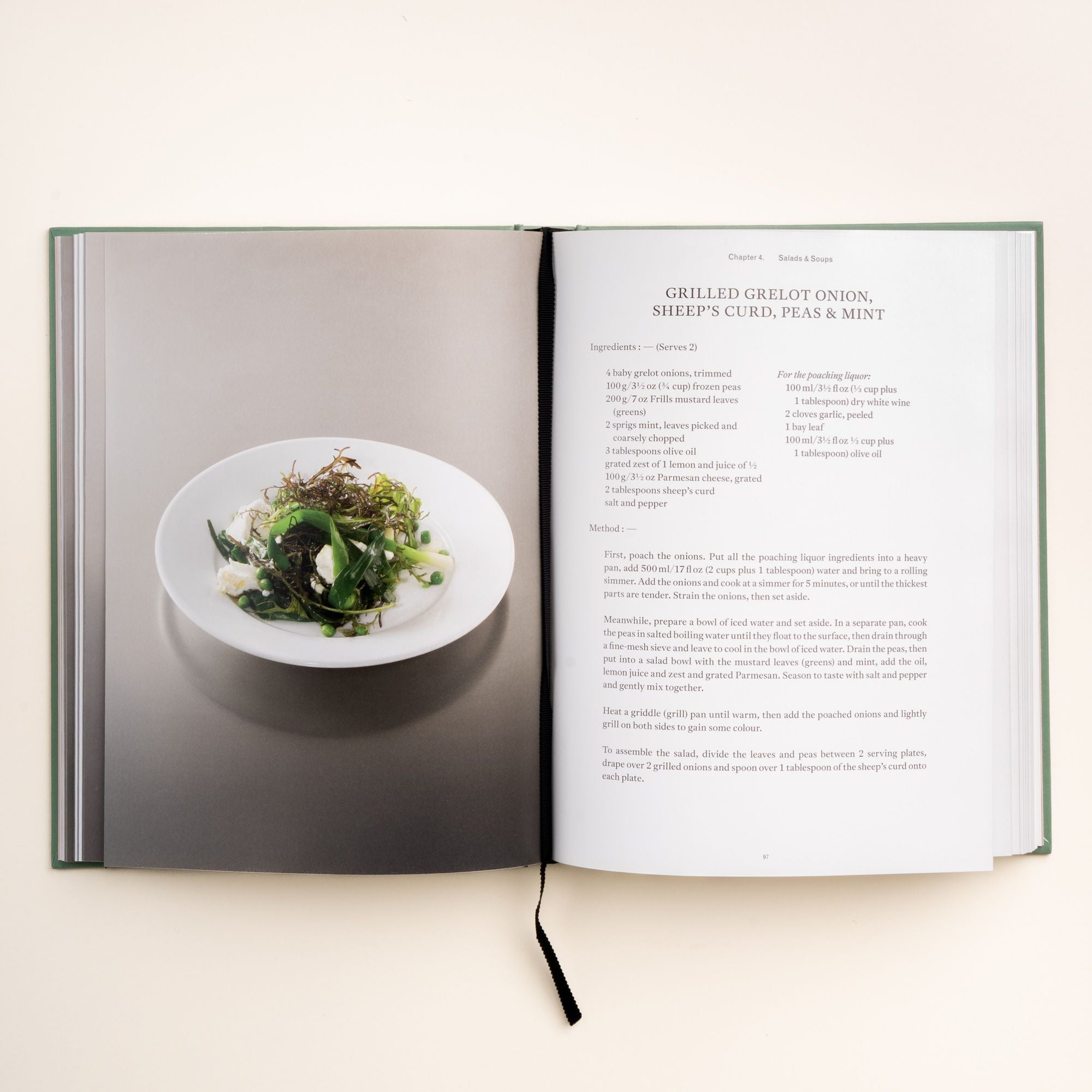 Open cookbook showing recipe for grilled grelot onion, sheep’s curd, peas, and mint with a plated salad on the left page.