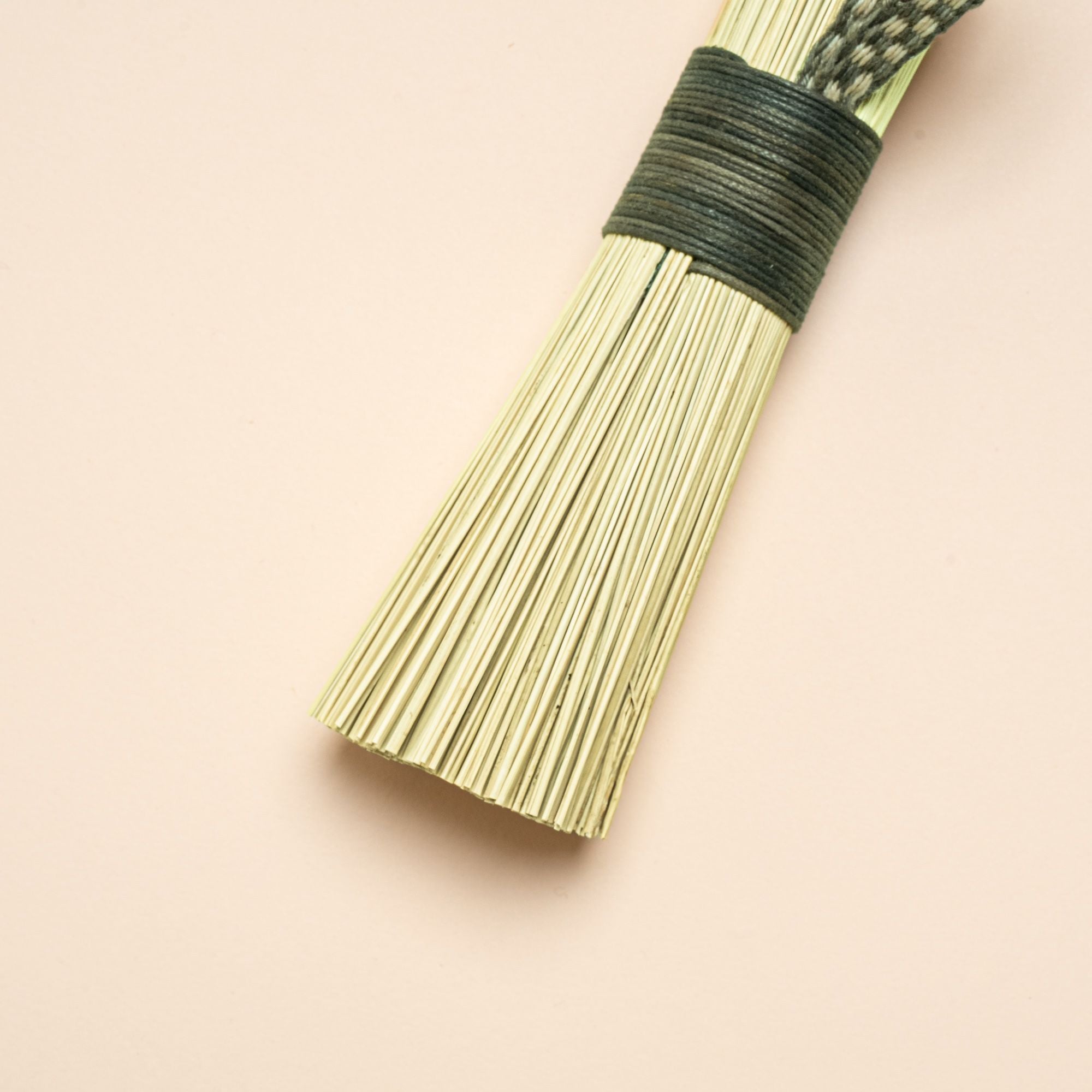 A closeup of a short scrub made out of broomcorn, tied together with cotton and a loop for hanging.