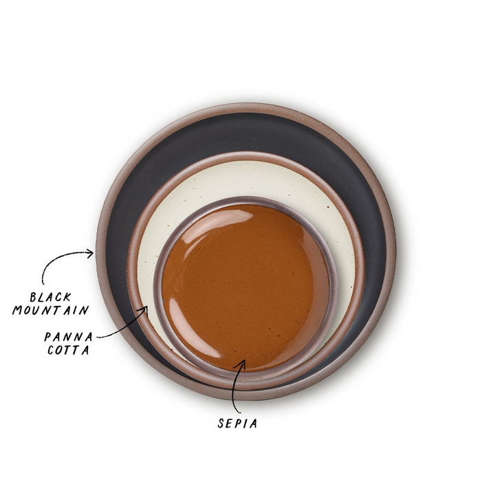 A stack of 3 plates in Dinner, Side, and Cake sizes in a black graphite, warm off-white, and glossy caramel brown colors.