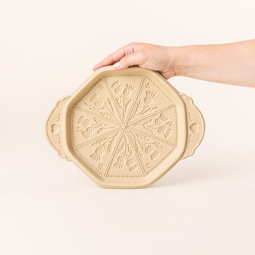 A hand holds up a shortbread pan with a thistle flower design on the bottom