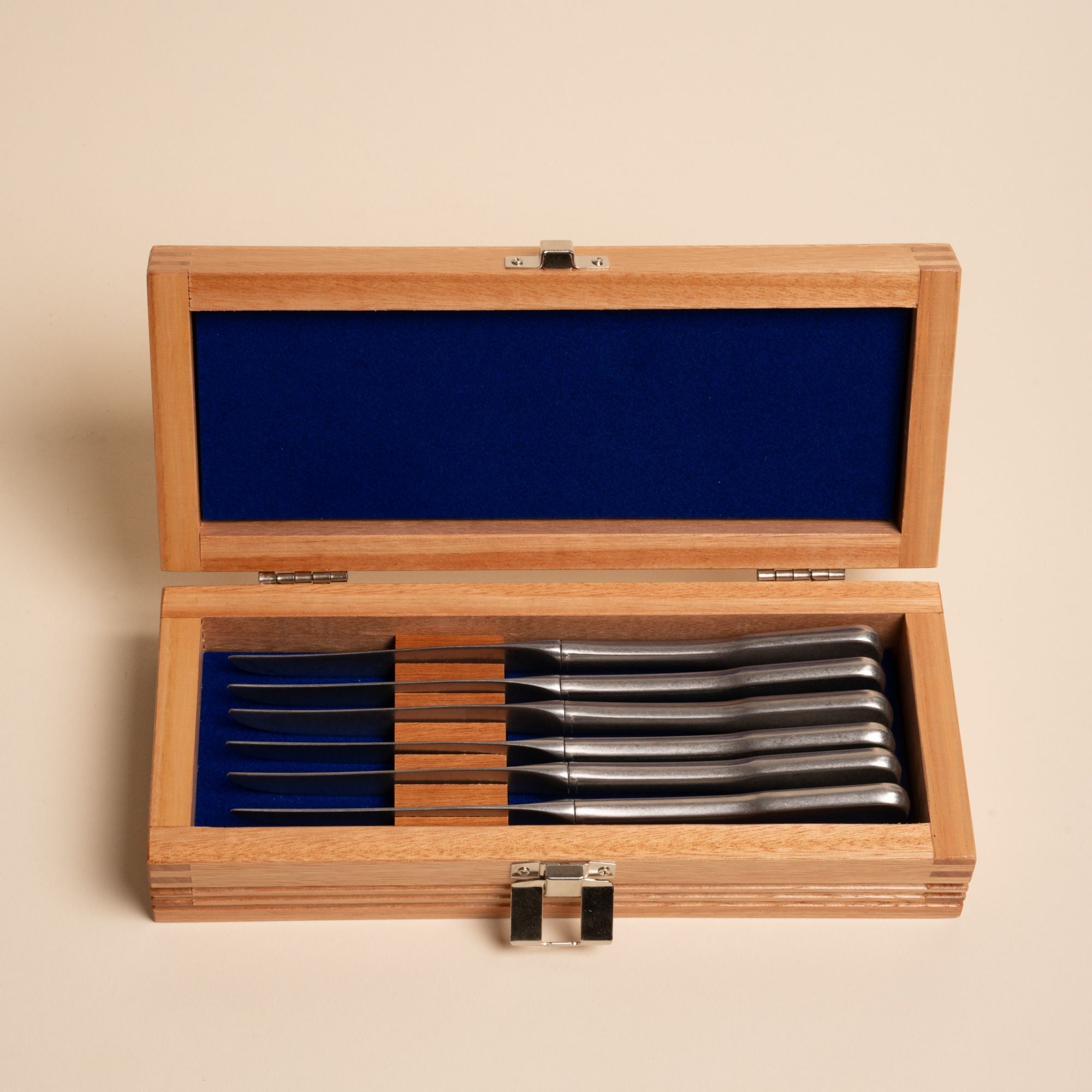 Set of six matte steel steak knives in a wooden box lined with deep blue fabric.