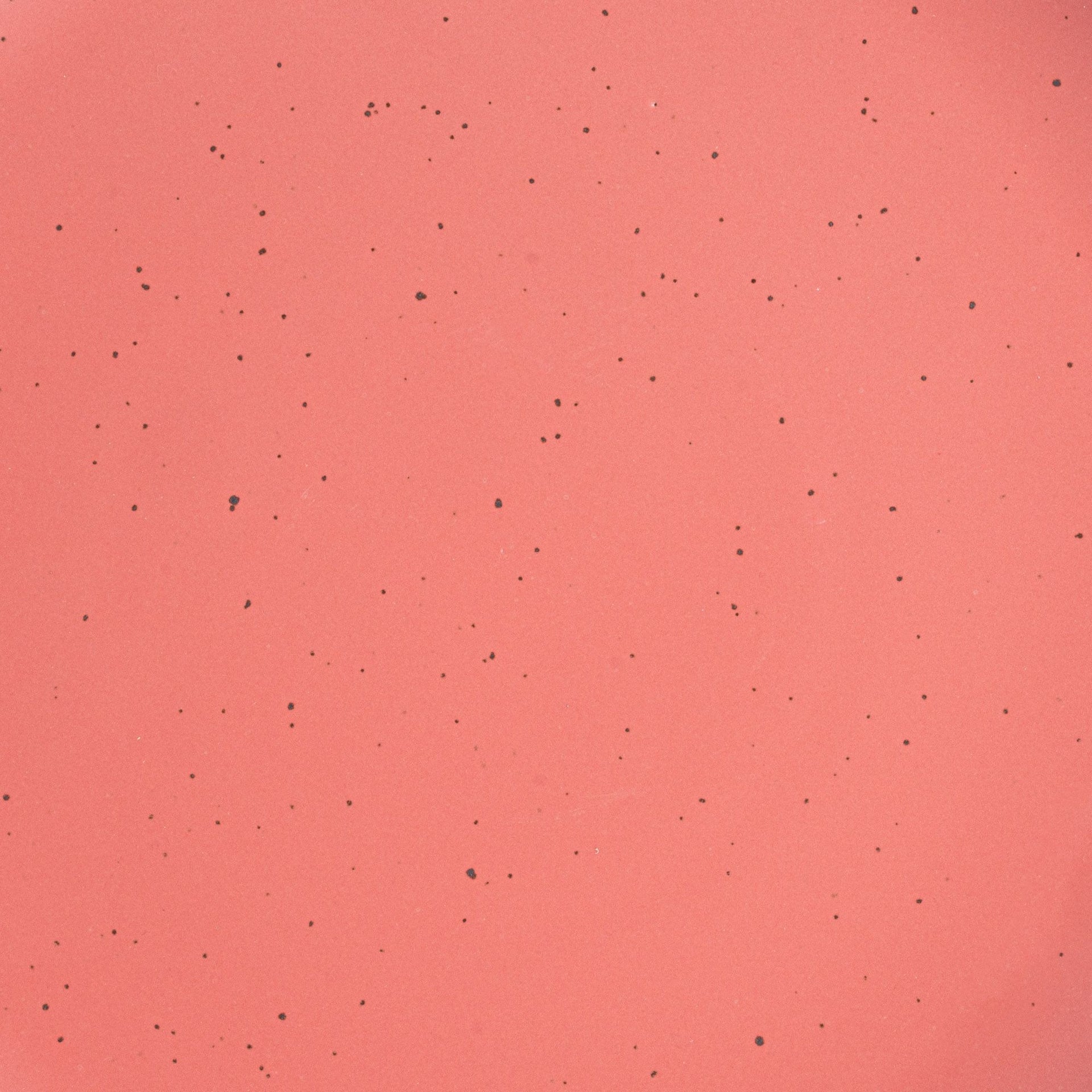 A closeup of a ceramic plate in a watermelon pink color with iron speckles throughout