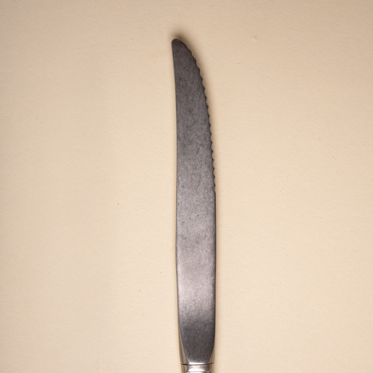 Close-up of a matte stainless steel steak knife with a serrated edge on a neutral background.