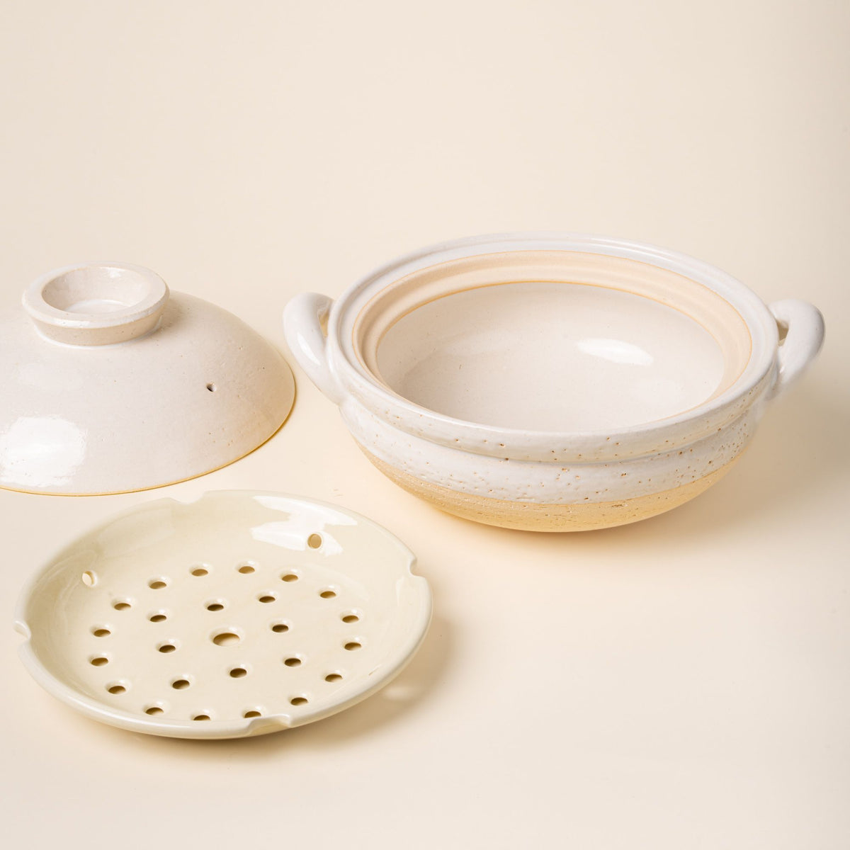 White ceramic donabe steamer with side handles, a steamer tray and a lid to the side.