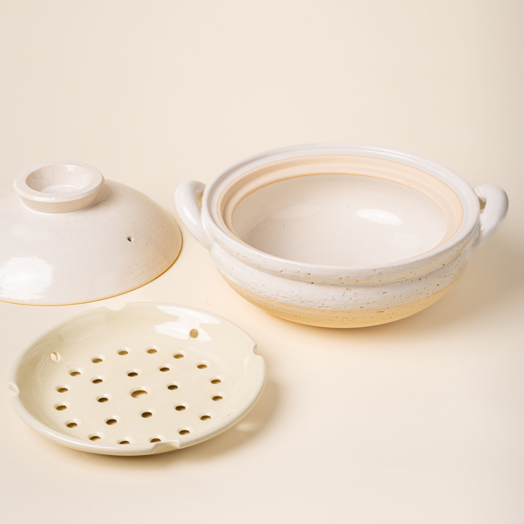 White ceramic donabe steamer with side handles, a steamer tray and a lid to the side.