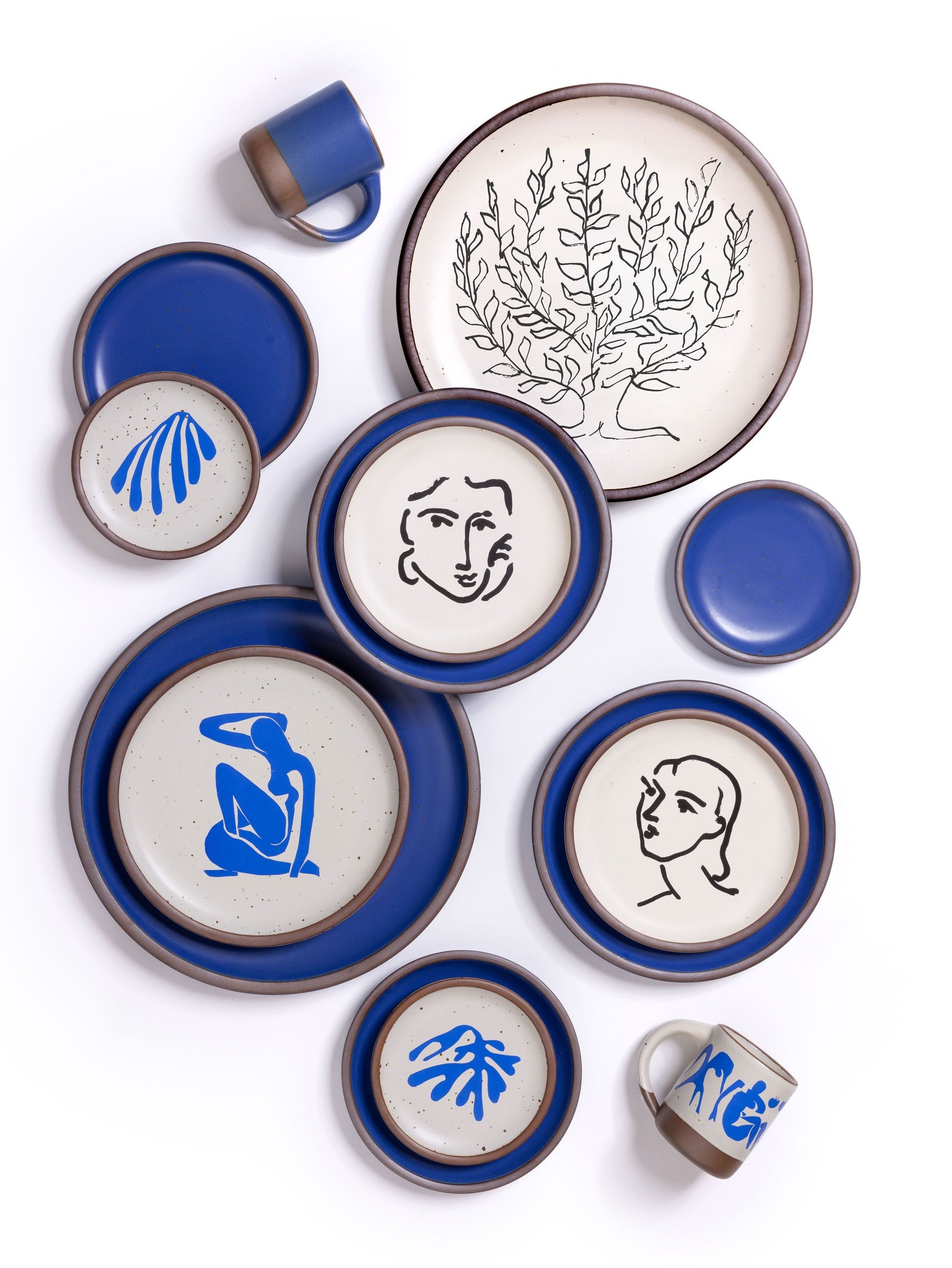 Ceramic plates and mugs with decals of Henri Matisse's artworks along with a cobalt blue plates and mugs on white background.