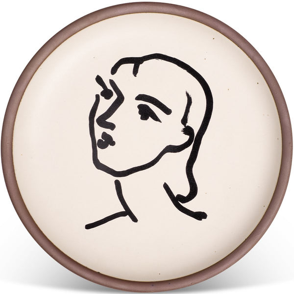 Circular ceramic plate with a cream background featuring a minimalist black line drawing of a person's face, bordered by a muted brown rim.
