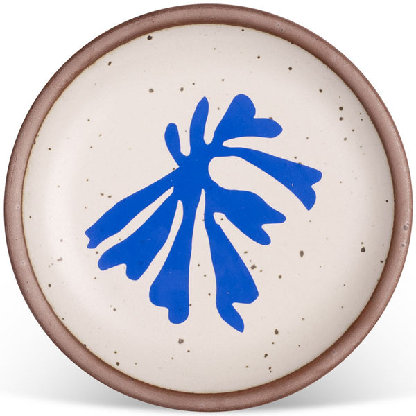 Round ceramic plate with a speckled off-white glaze and a bold abstract blue design in the center, bordered by a brown rim.