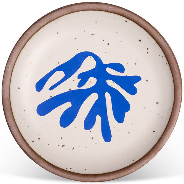 Round ceramic plate with a speckled white glaze and a bold blue abstract design in the center, edged with a natural brown rim.