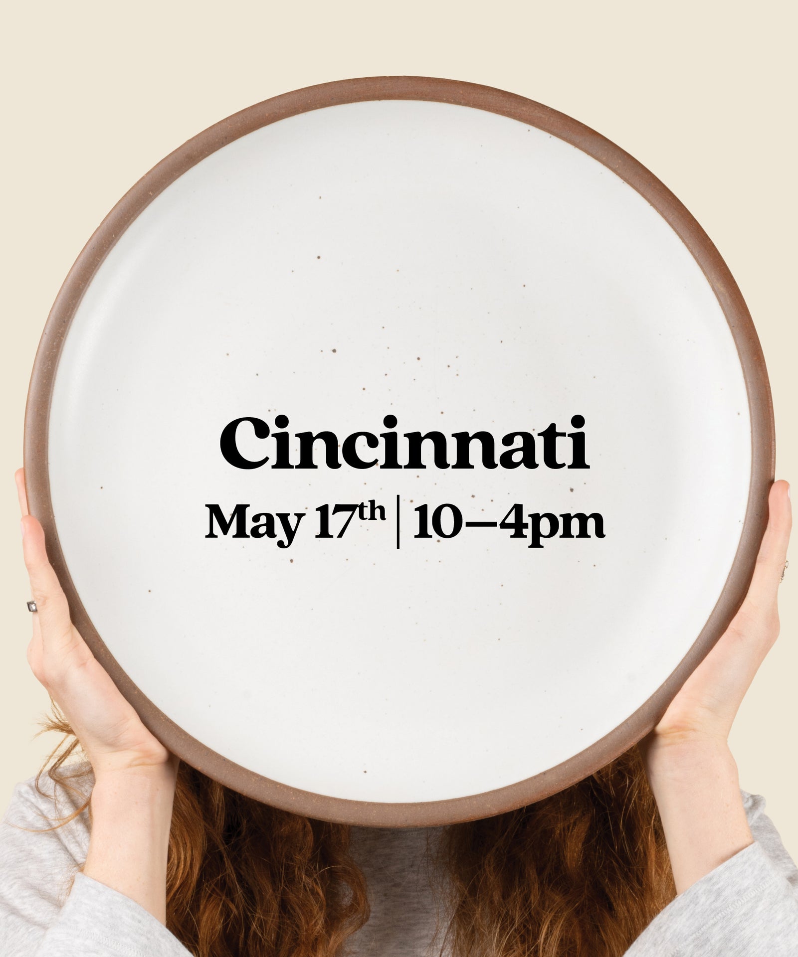 Person holding a round sign with 'Cincinnati May 17th 10-4pm' text.