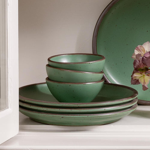 Set of green ceramic dinnerware with speckled texture on a white surface.