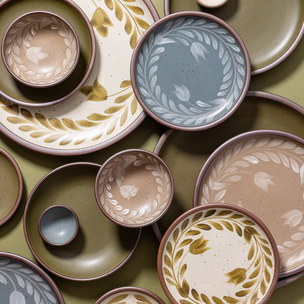 An overhead view of hand painted ceramic dinnerware featuring a tulip crown design against a green background.