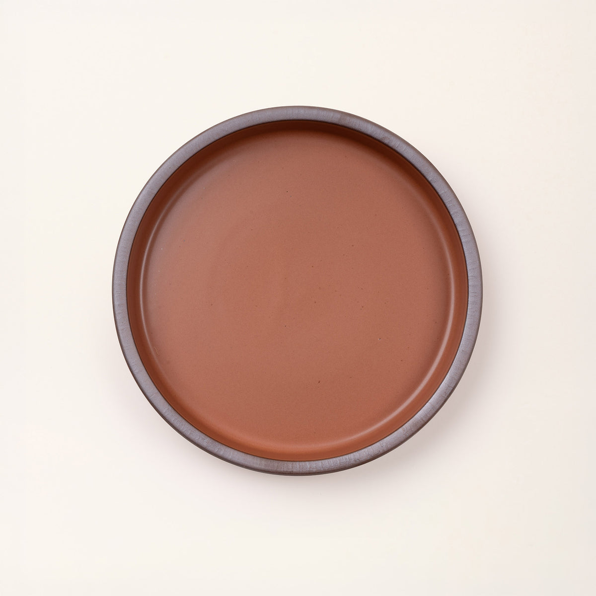 Overhead view of a shallow round ceramic baking dish in a matte cool terracotta color featuring an unglazed rim