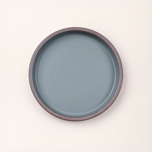 Overhead view of a shallow round ceramic baking dish in a matte blue-grey color featuring an unglazed rim