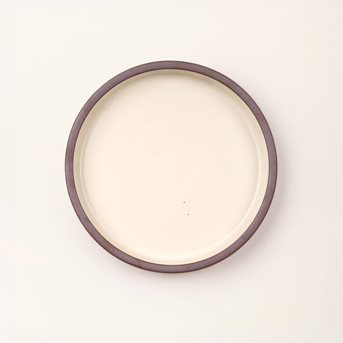 Overhead view of a shallow round ceramic baking dish in a matte warm off-white color featuring an unglazed rim