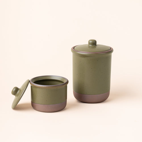 A small and tall ceramic lidded jars in a olive green color with an unglazed base.