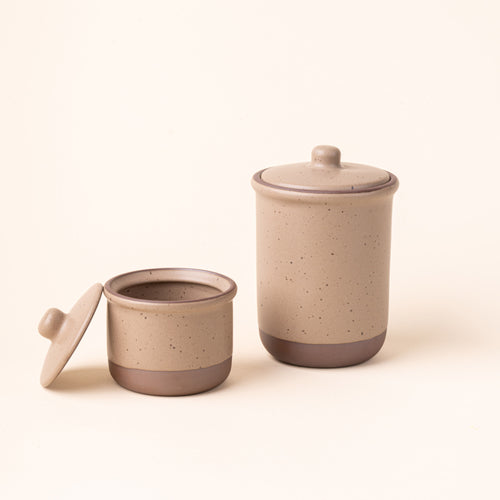 A small and tall ceramic lidded jars in a pale warm brown color with an unglazed base.