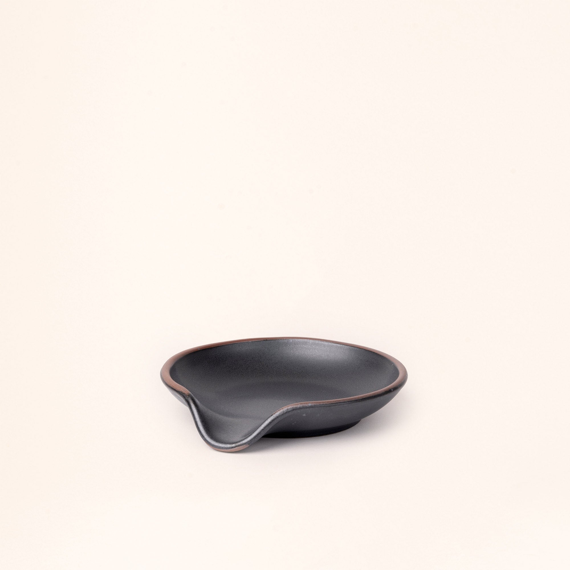 A side view of a ceramic spoon rest with a curved notch in a graphite black color with an unglazed rim.