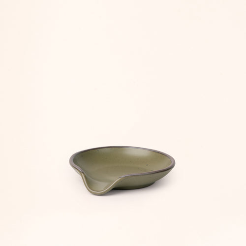 A ceramic spoon rest with a curved notch in an olive green color with an unglazed rim.