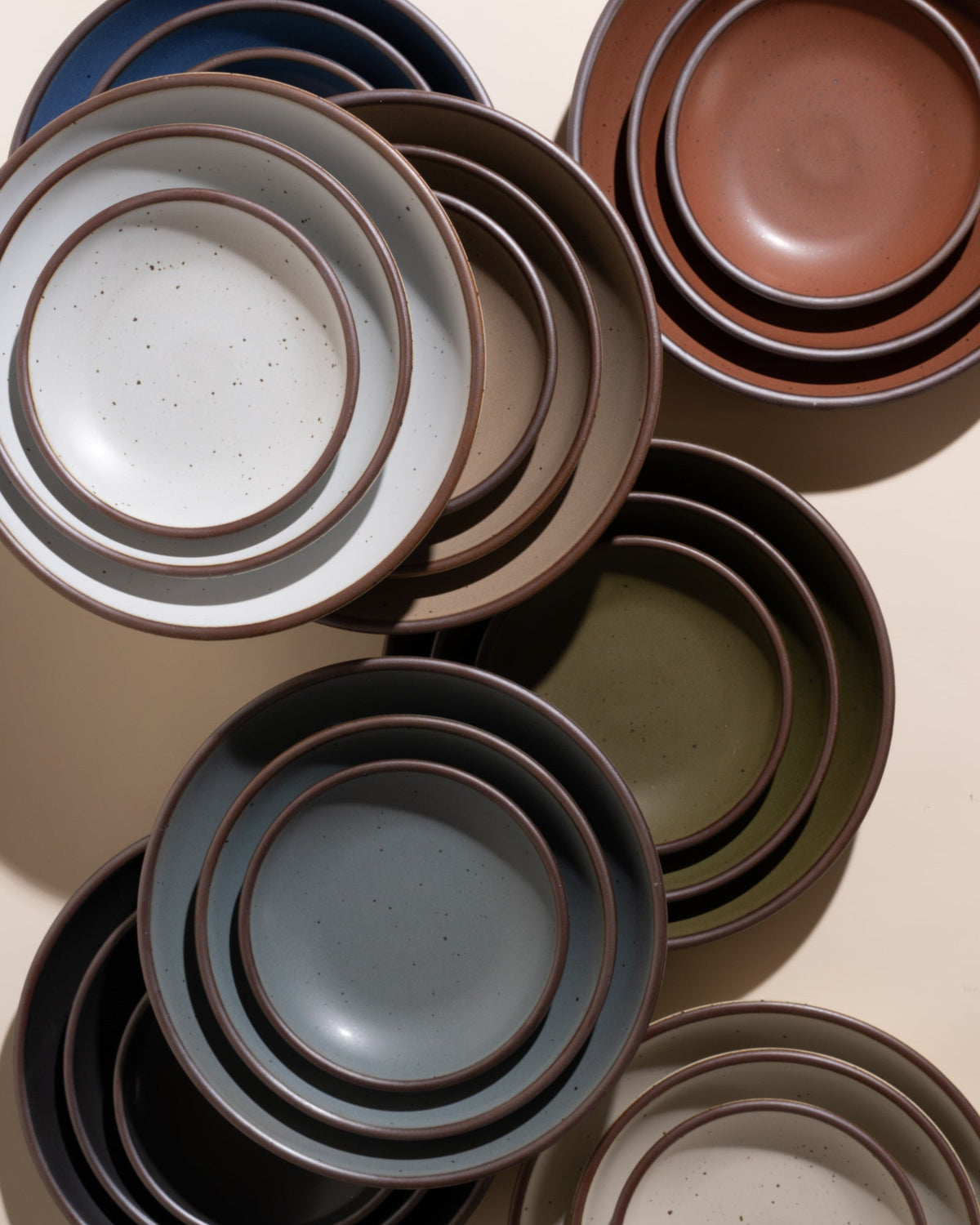 Stacks of ceramic plates in various colors on a neutral background