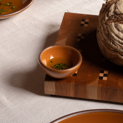Small earthy orange ceramic bowl beside a loaf of bread on a wooden cutting board.