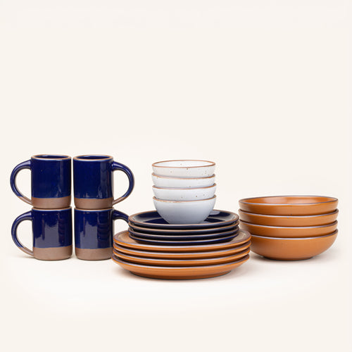 A 20-piece set of ceramic tableware, including mugs, bowls, and plates in a cool white, earthy orange, and glossy dark blue colors.