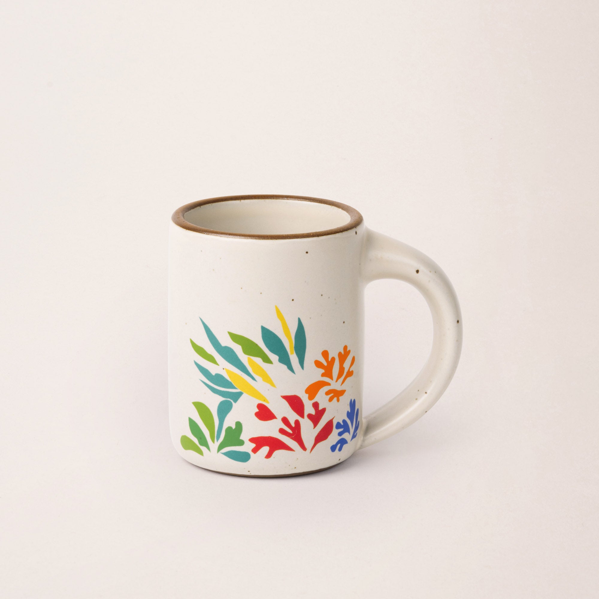 A full dip warm off-white mug with unglazed rim with colorful leaves decaled from Acanthes by Henri Matisse.