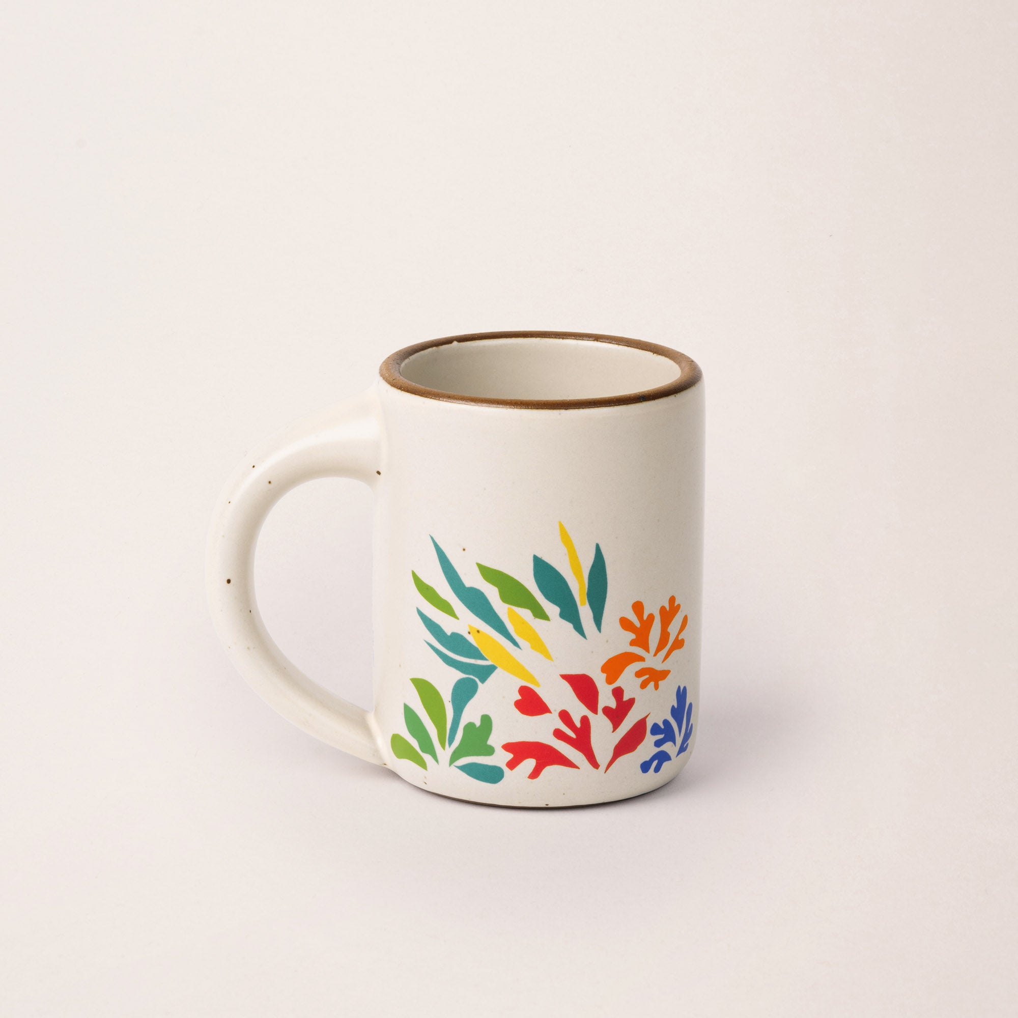 A full dip warm off-white mug with unglazed rim with colorful leaves decaled from Acanthes by Henri Matisse.