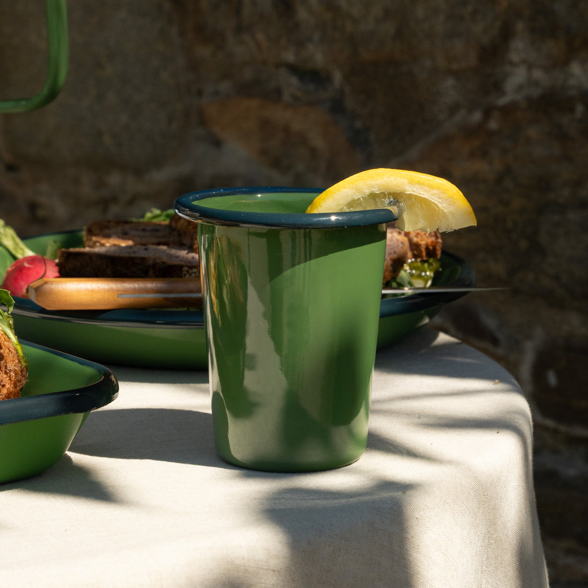 Green enamel short cup with lemon wedge on a table with food in the background