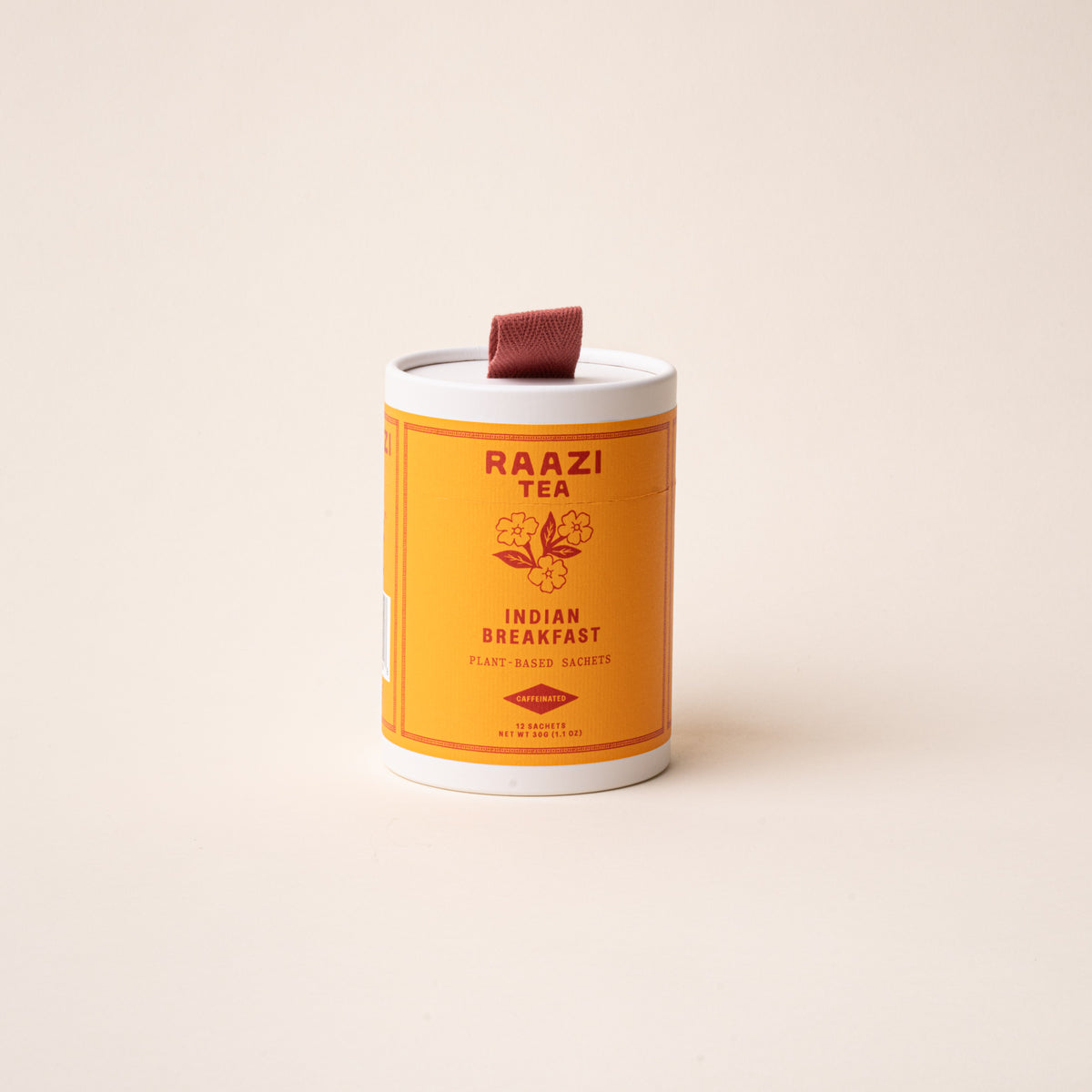 A white cylindrical tin of RAAZI Tea labeled 'Indian Breakfast’ with an orange label and small red pull tab, photographed on a pale beige background.