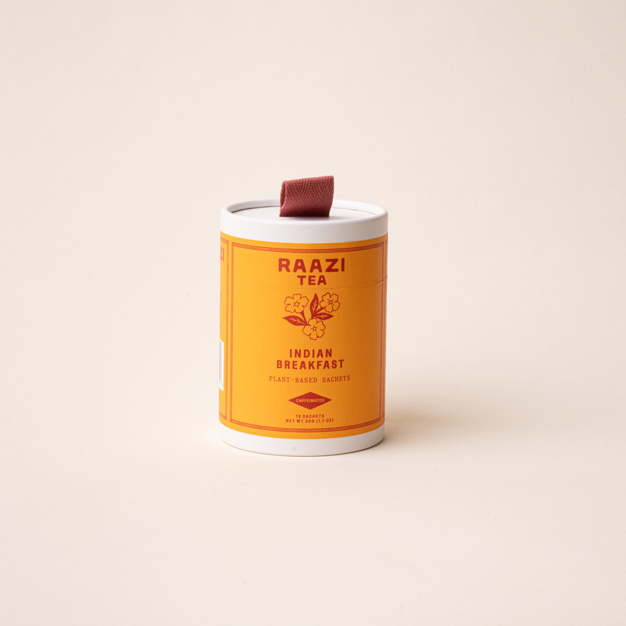A white cylindrical tin of RAAZI Tea labeled 'Indian Breakfast’ with an orange label and small red pull tab, photographed on a pale beige background.