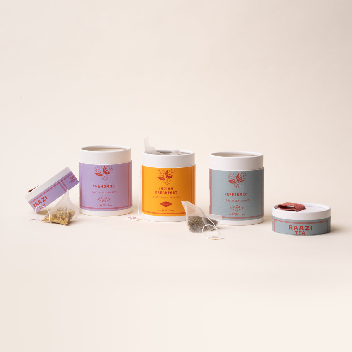 Three open RAAZI Tea tins (chamomile, peppermint, Indian breakfast) with loose sachets and lids on a neutral background.