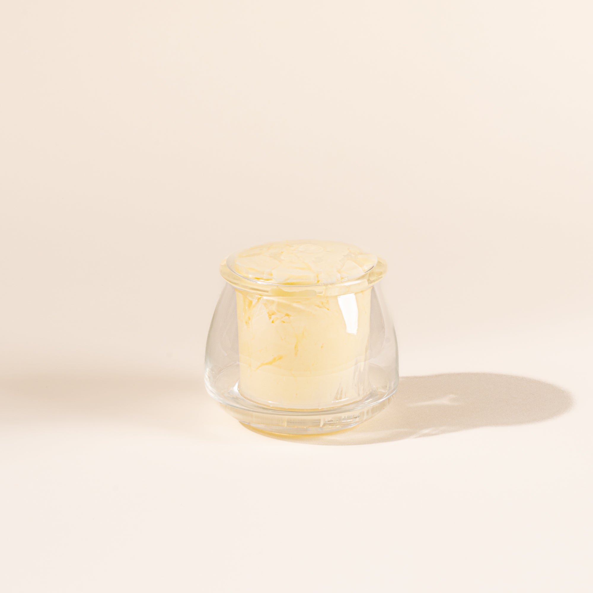 Clear glass butter keeper on white background, filled with butter