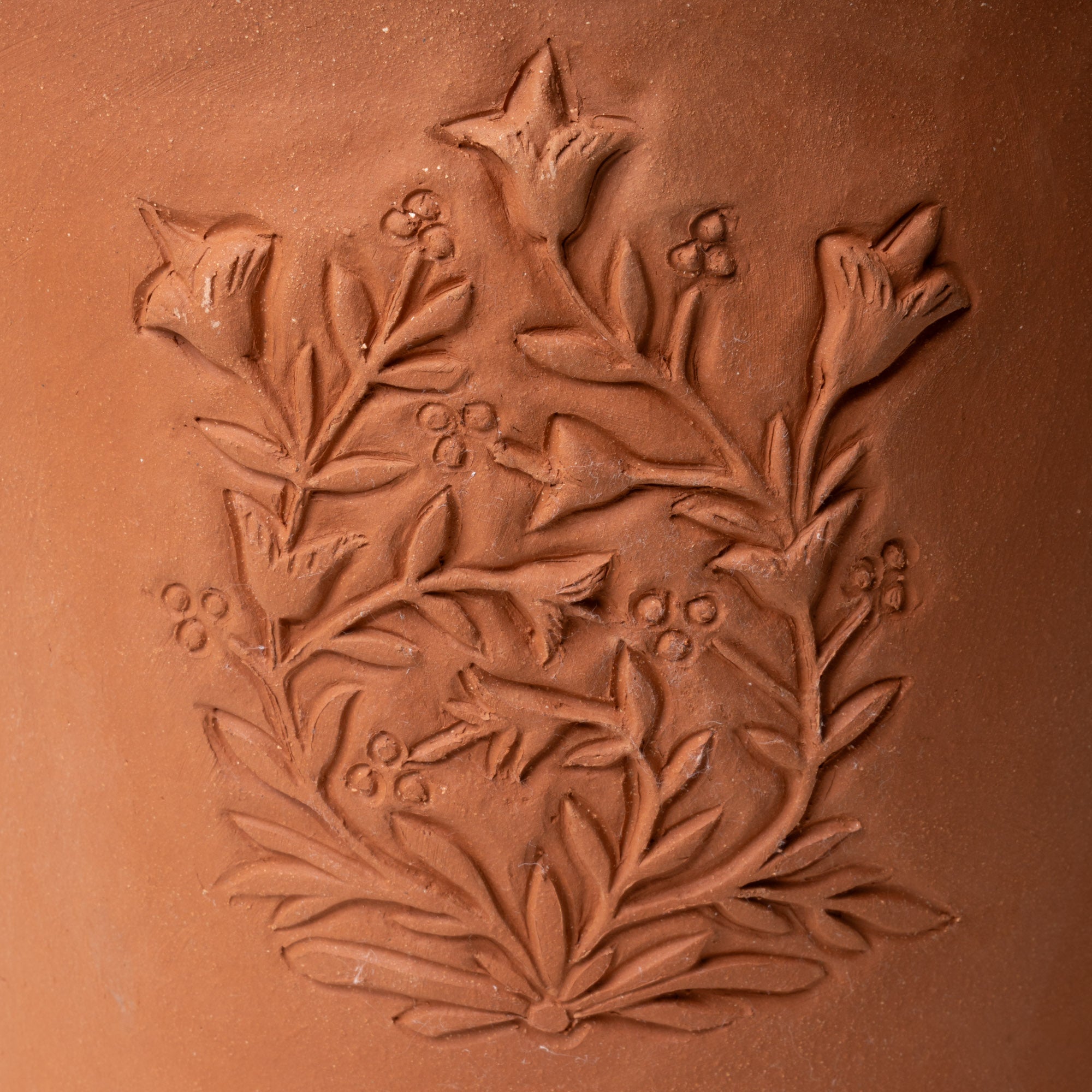Close up of an embossed floral design on a large terracotta flower pot.