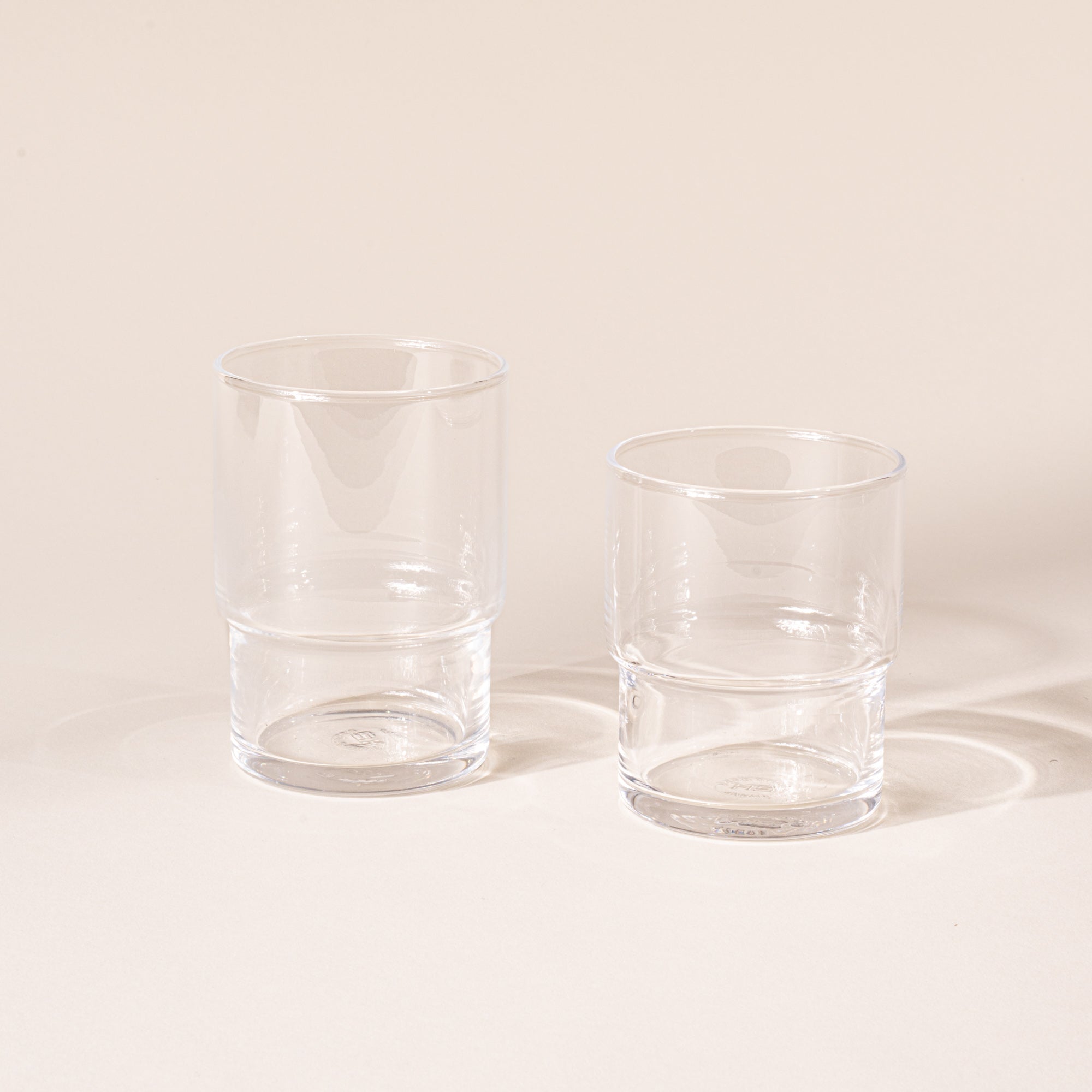 A small and medium clear cylindrical glass with a wider top half with a narrower bottom half