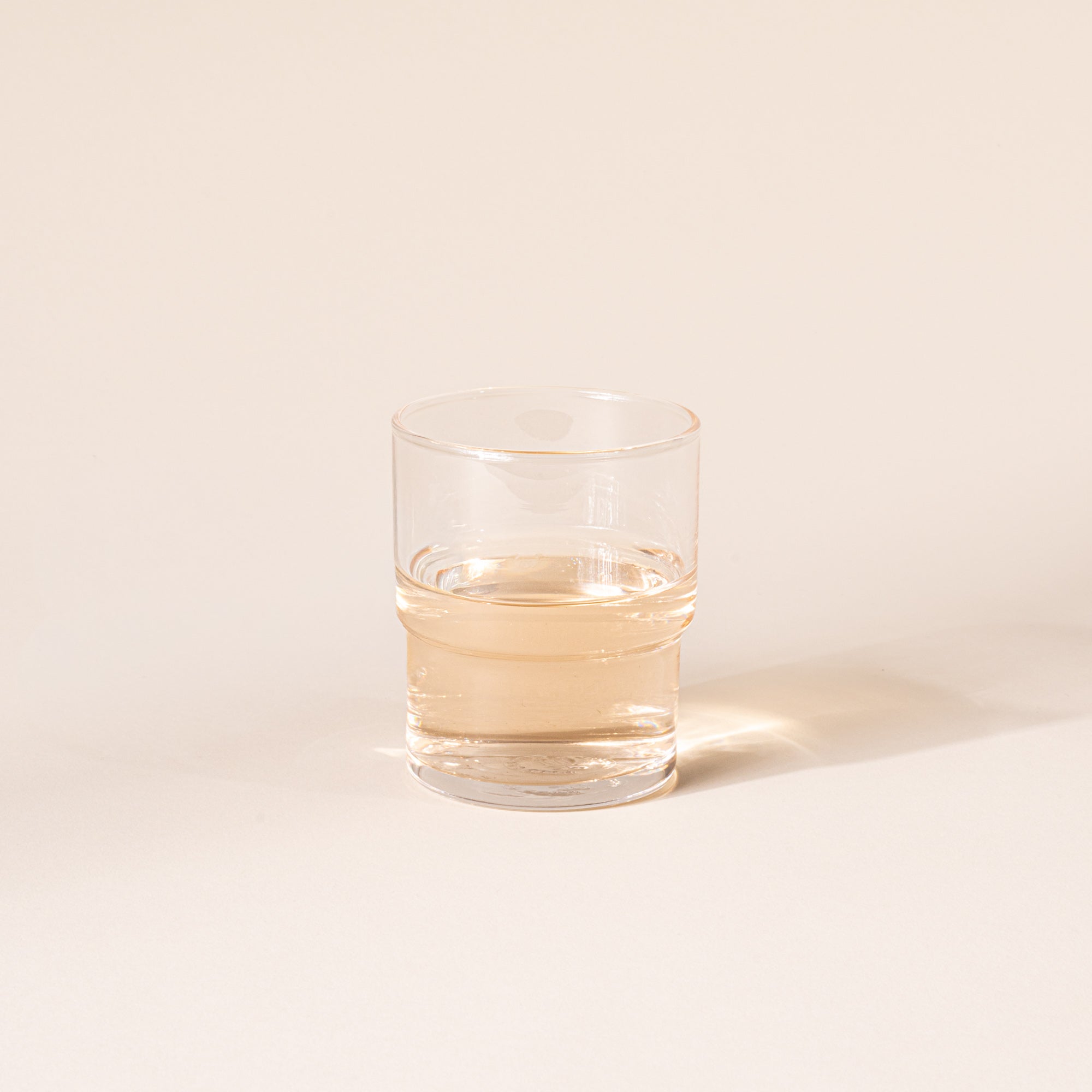 Clear cylindrical glass with a wider top half with a narrower bottom half, filled with a drink.