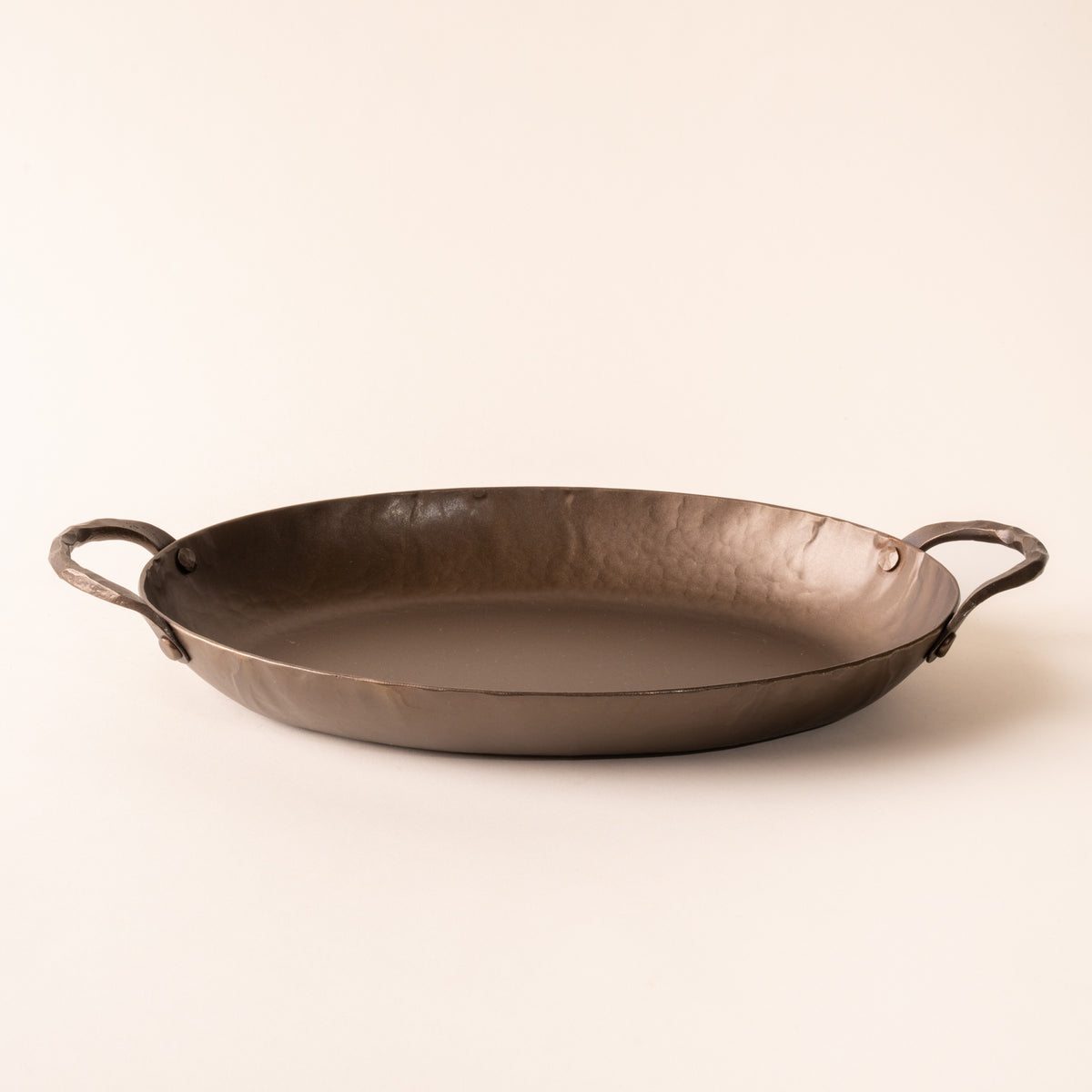 A hammered metal oval roasting pan with handles on both sides