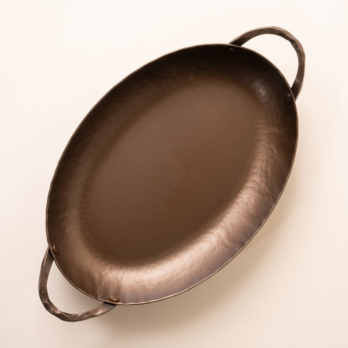 An overhead view of a hammered metal oval roasting pan with handles on both sides