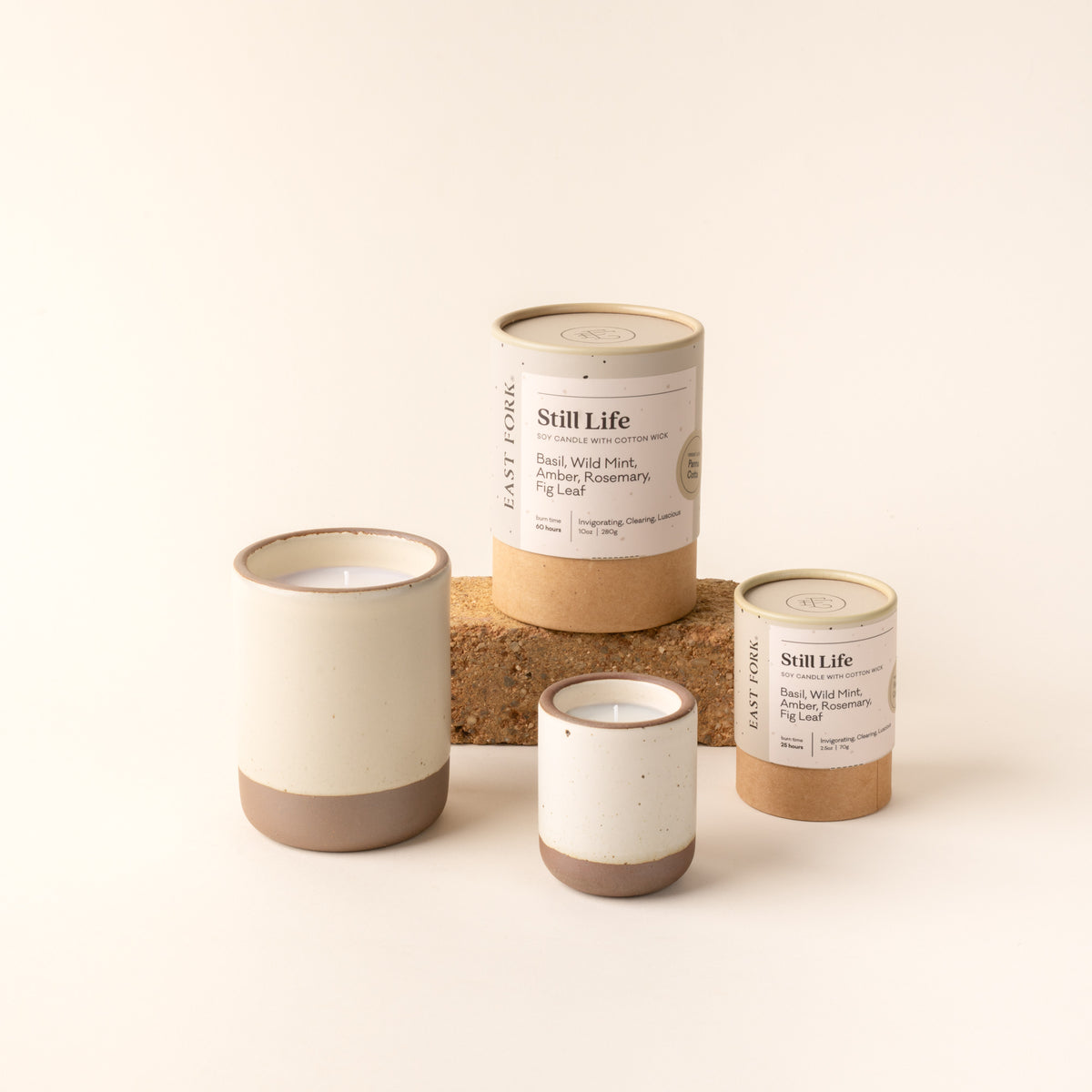 Small and large ceramic vessel in a warm off-white color with candles inside, arranged with tube packaging that reads 'Still Life'