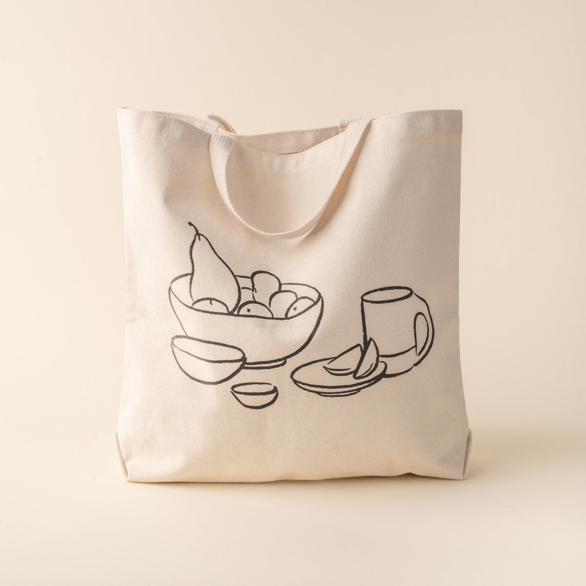 A beige cotton tote bag with a black printed drawing of a bowl and a mug