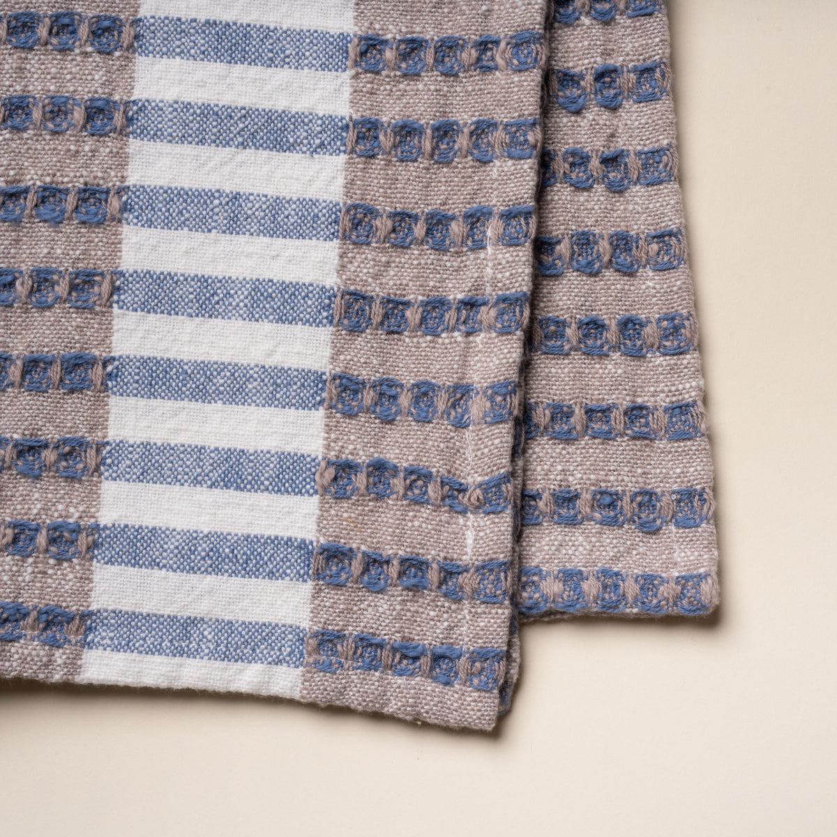Closeup of the weave of a folded woven kitchen towel with blue and beige striped pattern on a light background.