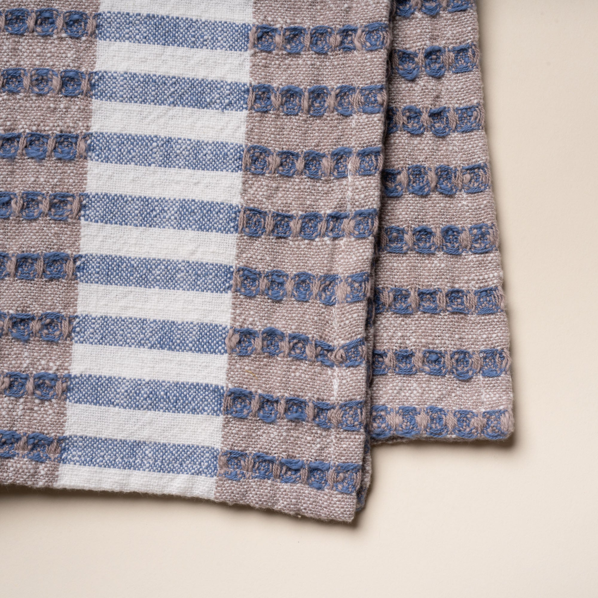 Closeup of the weave of a folded woven kitchen towel with blue and beige striped pattern on a light background.