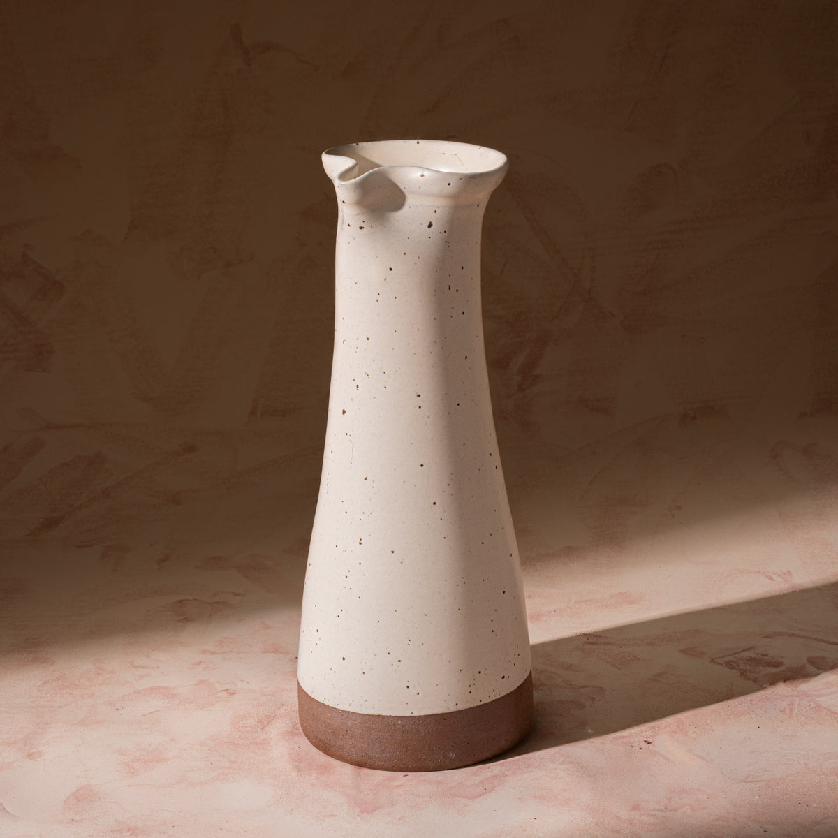 Tall ceramic carafe in an off-white color with iron speckles and an unglazed base.