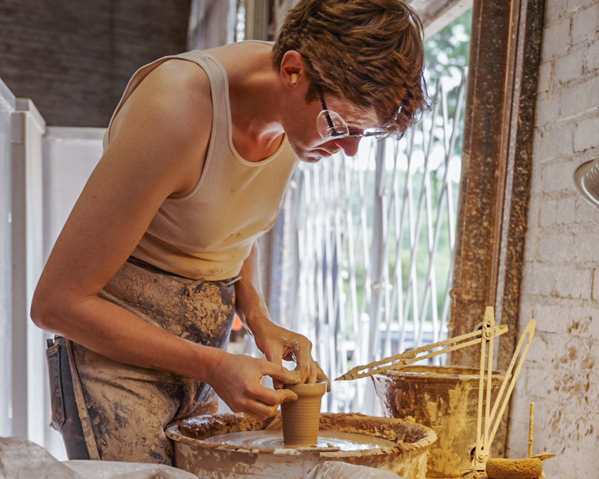 Person working with clay on a pottery wheel in a studio setting.