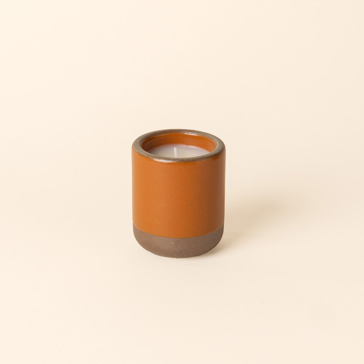 Small ceramic vessel in an earthy orange color with candle inside.