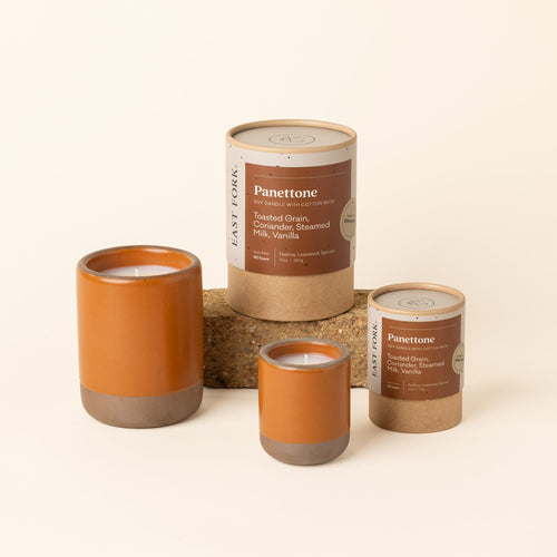 Small and large ceramic vessels in an earthy orange color with candle inside each with packaging.